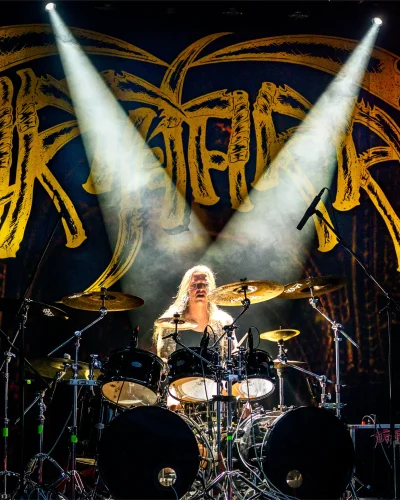 Large stage backdrop with a band logo behind a drummer on a concert stage