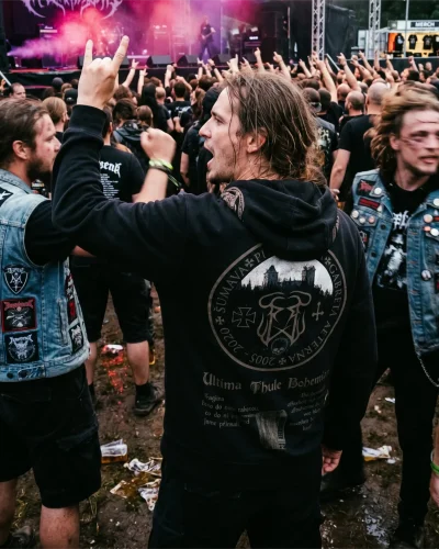 Pohled zezadu na dav na metalovém festivalu s lidmi v černých mikinách a vestách s nášivkami
